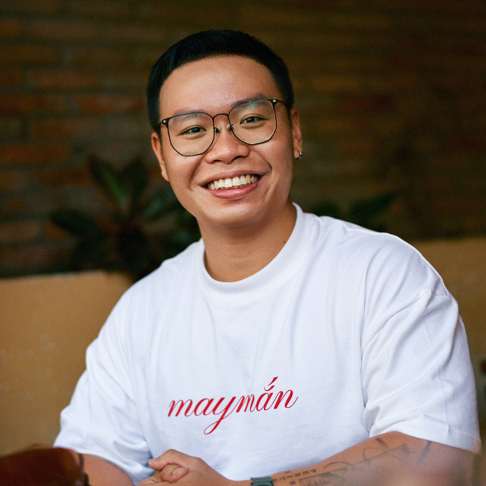 In the image, the photographer is smiling at the camera, wearing a white T-shirt with red text. The word on the T-shirt is “lucky” in Vietnamese.