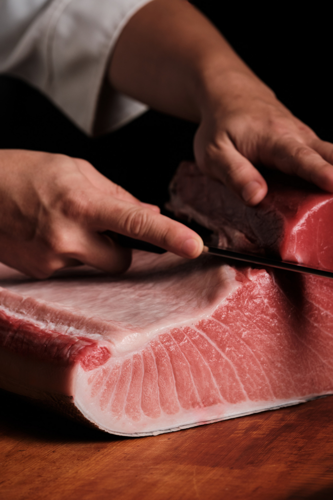 A close-up of hands slicing fresh fish on a wooden cutting board.