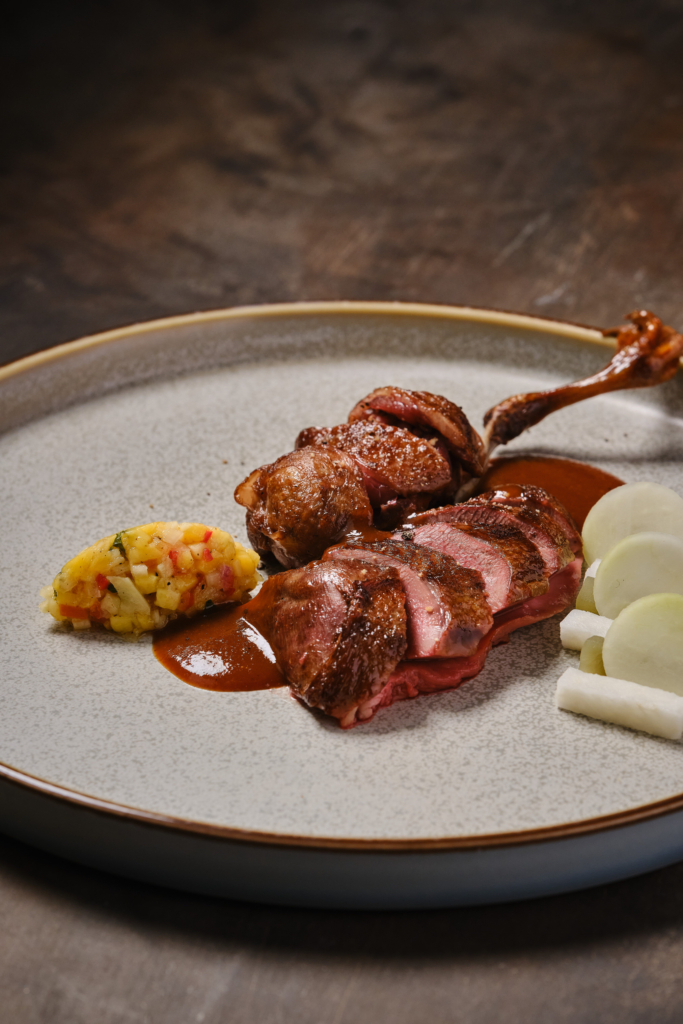A plated meat dish with sauce and vegetables, photographed on a neutral background.