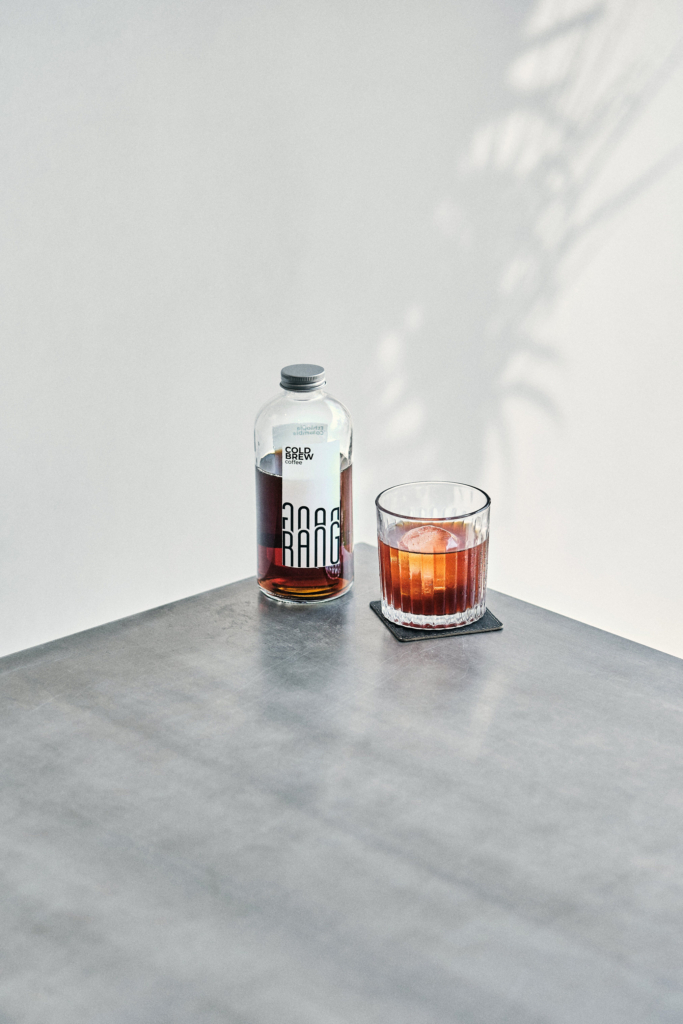 A bottle and a glass with a dark drink placed on a minimal tabletop.