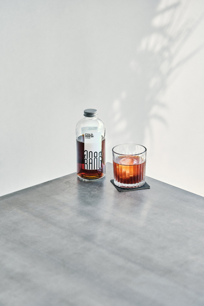A bottle and a glass with a dark drink placed on a minimal tabletop.