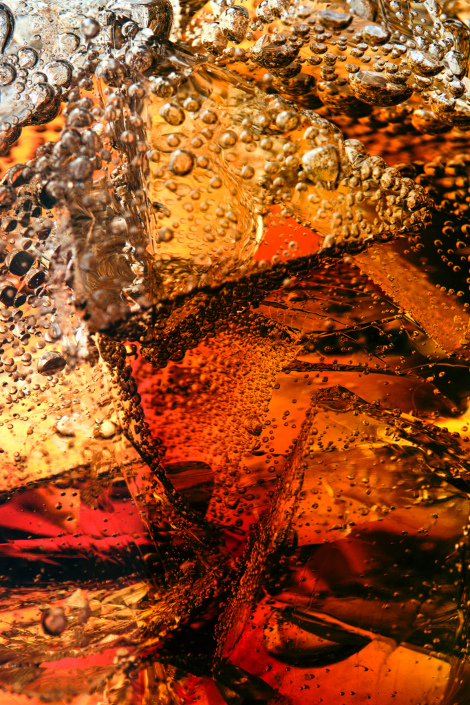 An abstract close-up of ice and bubbles suspended in amber liquid, where light, texture, and movement collide.