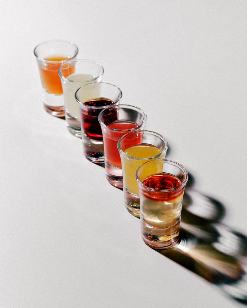 A row of small glasses filled with colorful drinks on a light surface.