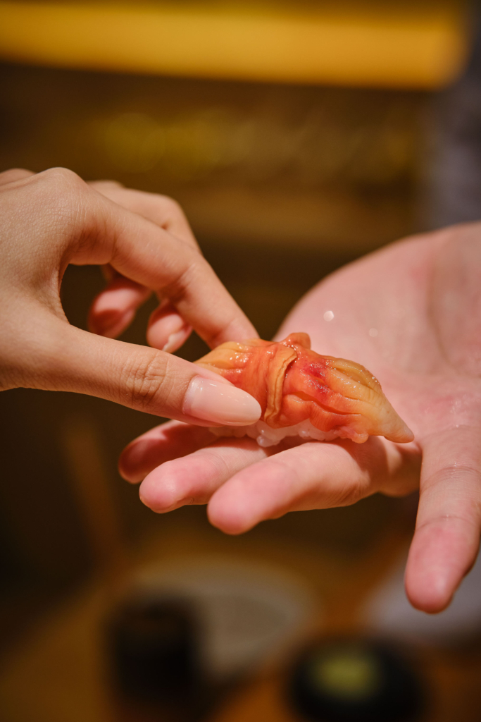 A piece of food being gently placed on an open hand, photographed in warm light.