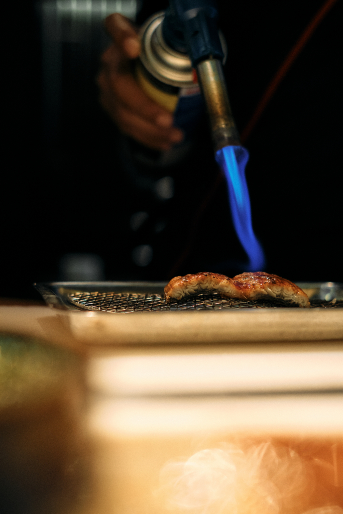 A blowtorch flame searing food on a metal surface.