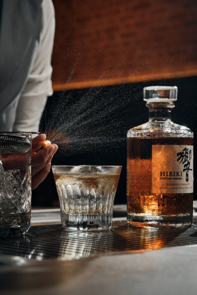 A fine citrus mist floats over the glass as Japanese whisky catches the light — precision, aroma, and ritual in one quiet moment.