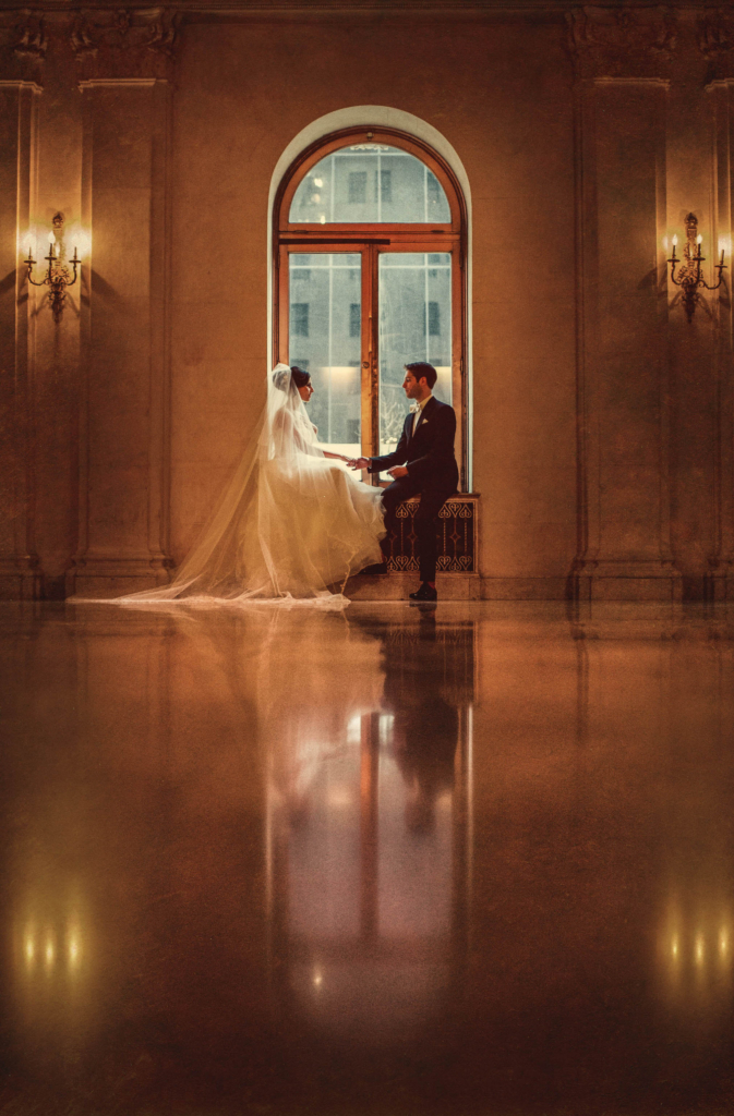 When you think of luxury in Manhattan you think of the Plaza. It derives its’ name from its’ location at the corner of Grand Army Plaza, right at the junction of Central Park South and Manhattan’s iconic Fifth Avenue. In 1969, the Plaza was given status as a landmark by the New York City Landmarks Preservation Commission. In 1986, it was named as a National Historic Landmark. From the Palm Court’s stained glass ceilings to the delicacy of the Champagne bar, the Terrace Room to the Edwardian Room, the Plaza is the epitome of class and luxury. I love photographing weddings at this sumptuous hotel. The suites are superb, the lighting is lovely, and there are many, many locations to create exquisite portraits. At this 2014 winter Plaza wedding the bride and groom braved the cold for some portraits, but we ended up inside to finish out their portrait session. I absolutely adore this image of them simply sitting in this window. I got as close to the ground as I possibly could so that I could capture the reflection in the floor as clearly as I was able. I love the mirrored image in the floor. I love the gorgeous lighting coming from the window and how it matches the warmth of the Plaza walls. Most of all I love the sweetly natural interaction between the bride and groom. Without that the portrait would not be as impactful!