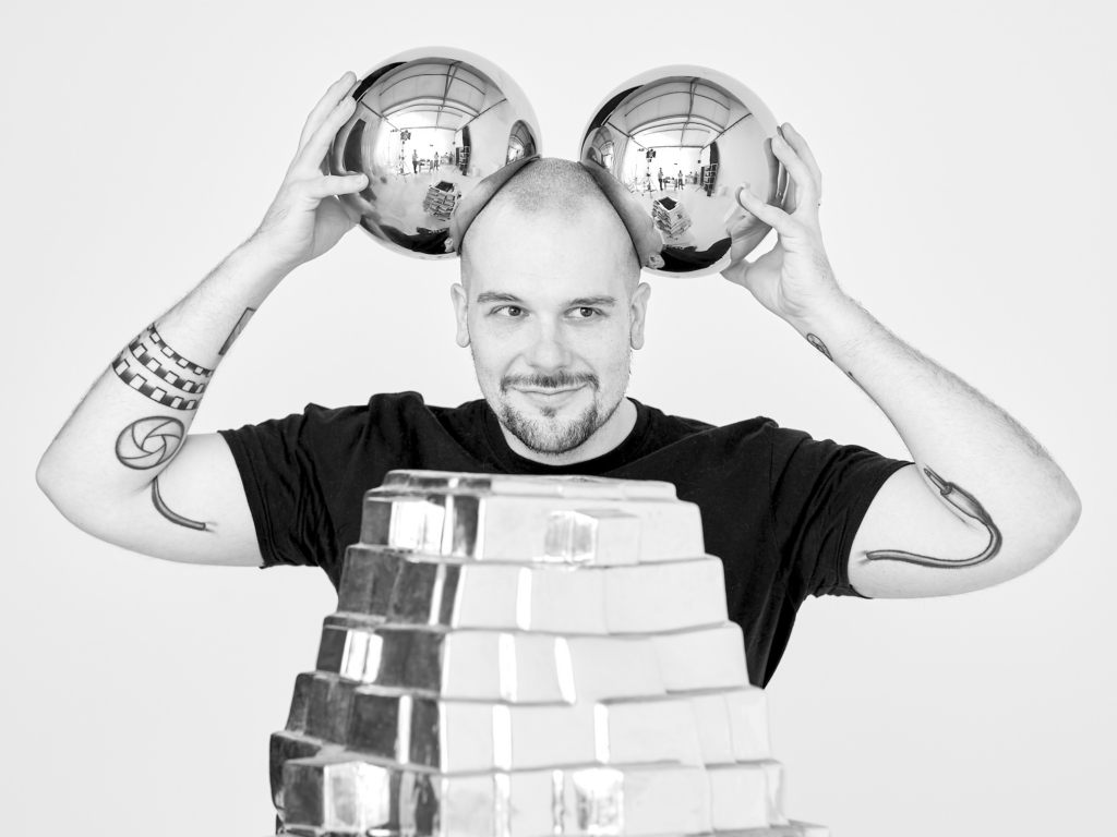 A photo on black and white of Konstantin Odin holding two silver balls next to his head. 