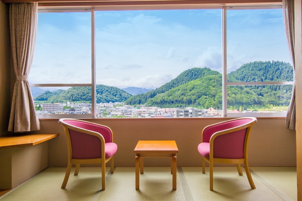 a photo of two chairs by the windows faceting one another  - the chairs are red and the view is a green mountains. 