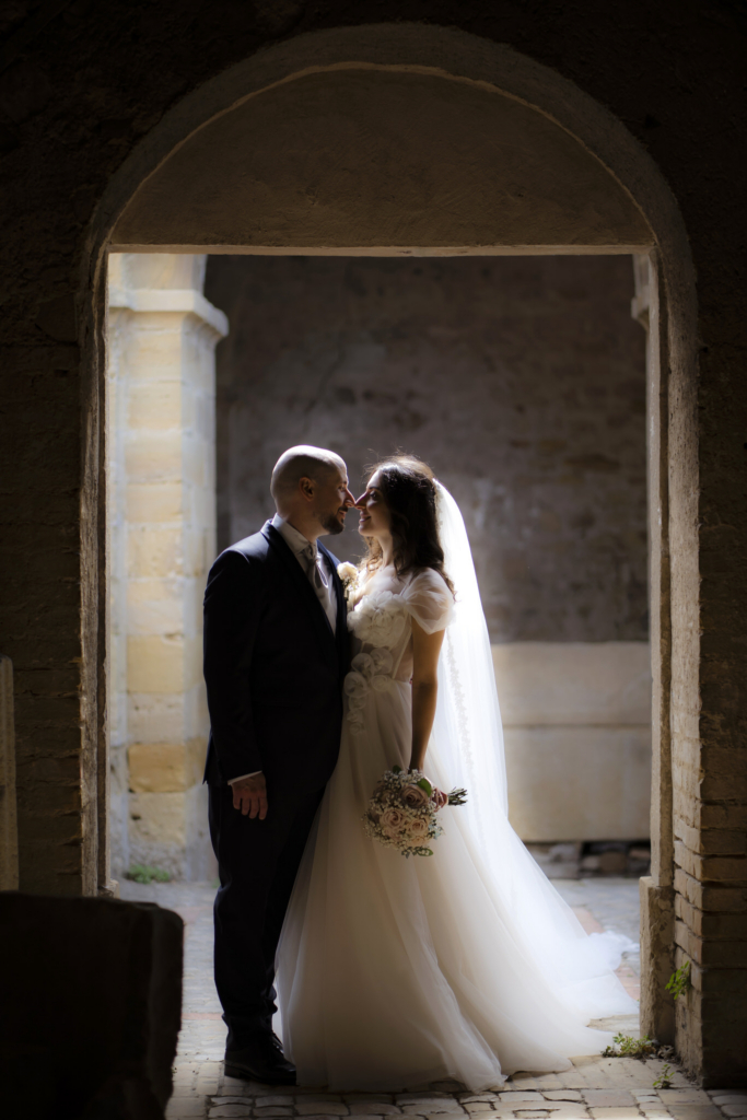 Bride and groom standing close under an archway, softly lit in an intimate wedding moment.