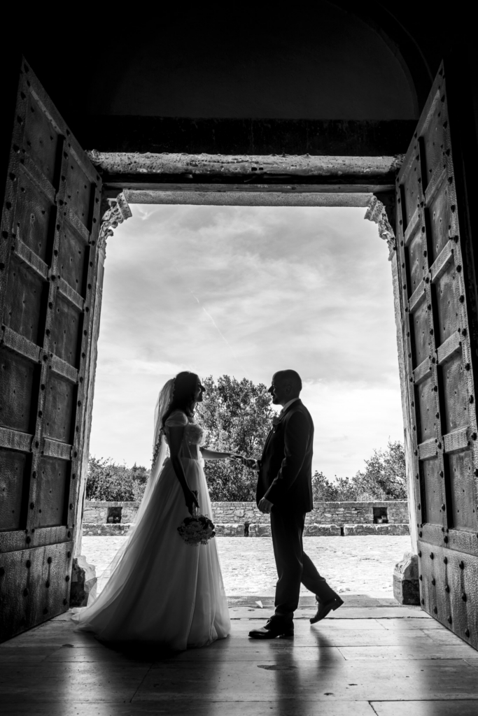 Bride and groom silhouetted in a doorway, meeting between shadow and light.