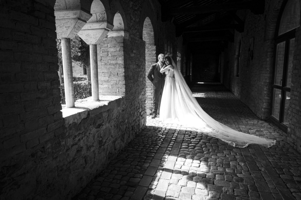 Bride and groom embracing in a dramatic play of light and shadow beneath stone arches.