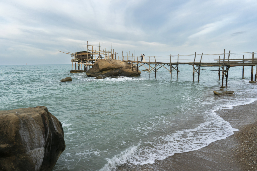 Wooden fishing structure on stilts extending into the sea along a quiet coastline.