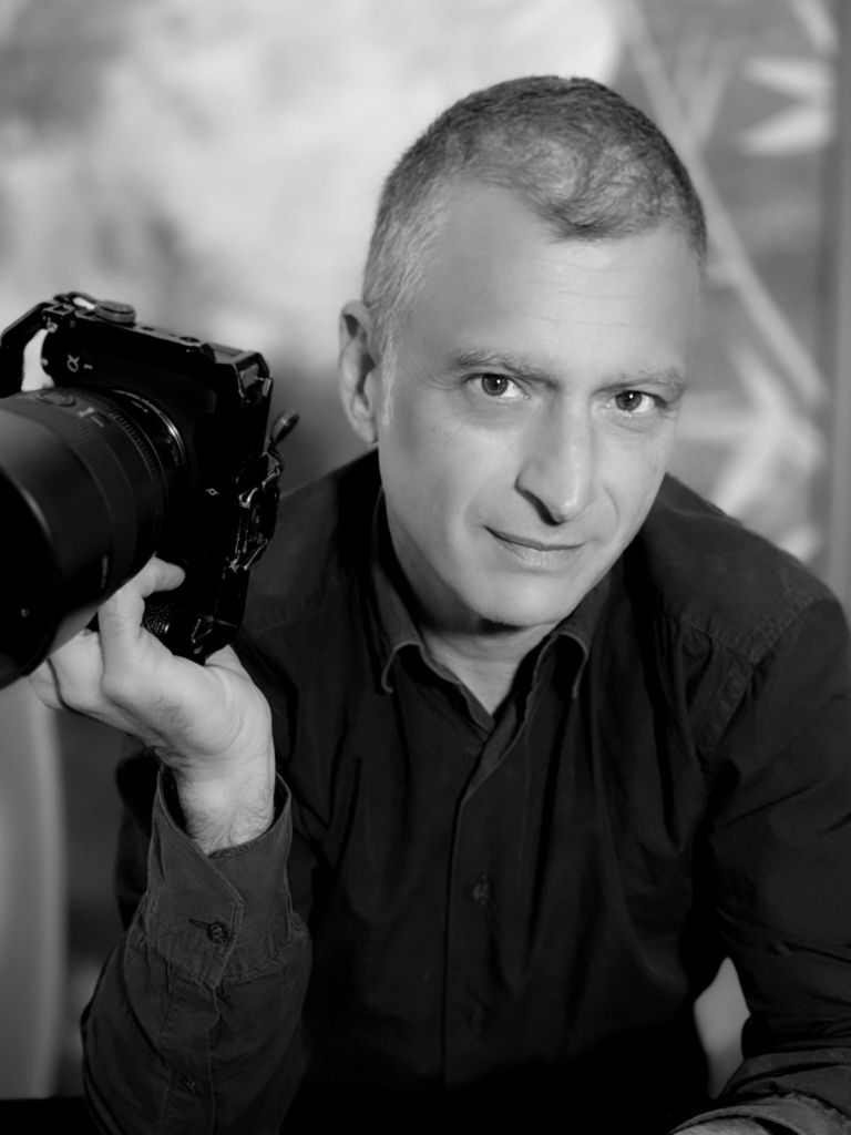Portrait of photographer David Melfi holding a camera, looking directly at the viewer.