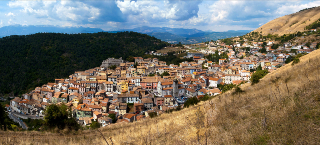 Panoramic view of a hillside village with colorful houses surrounded by mountains and open landscape.