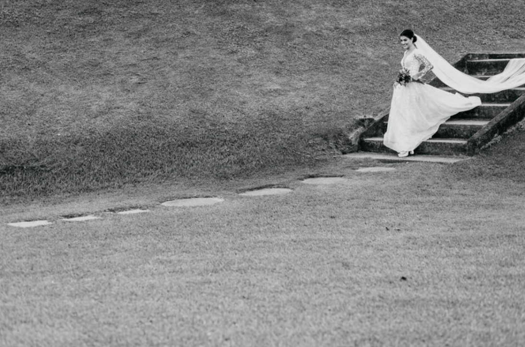 A bride in a long gown walks down a set of outdoor steps, her veil flowing behind her.