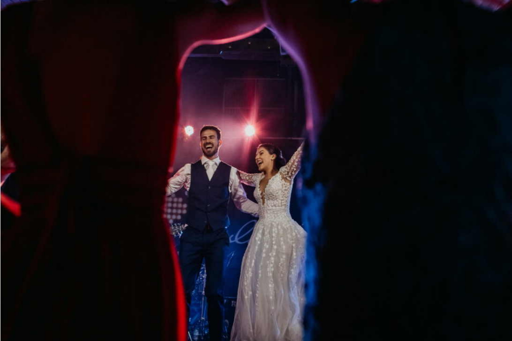 A couple celebrates on a dance floor under colorful lights, smiling and raising their arms during a lively moment.