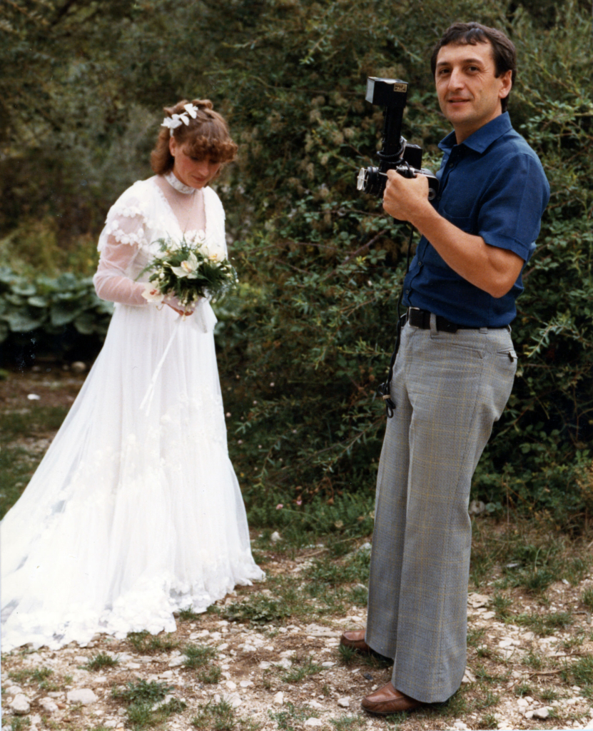 David Melfi’s father photographing a bride with a vintage camera, capturing a wedding moment outdoors.