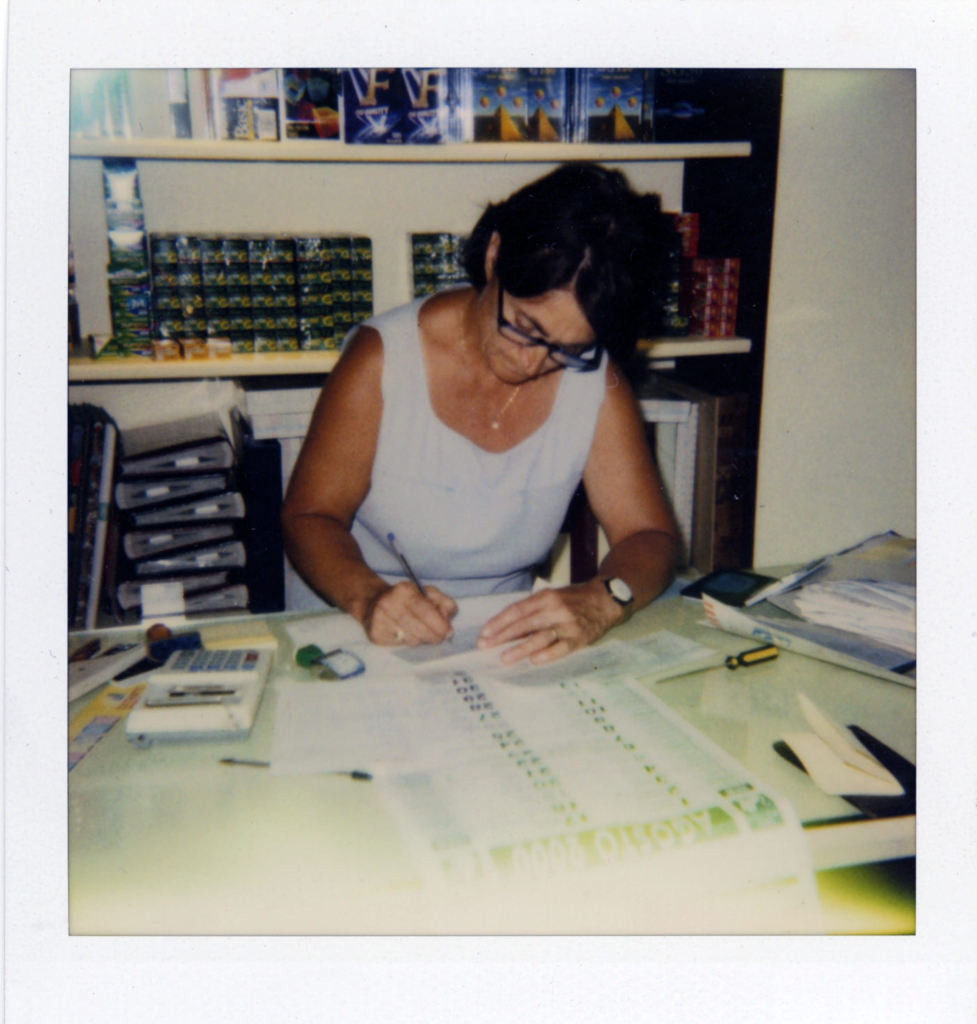 Photographer’s mother working at a desk, carefully handling prints and studio materials.