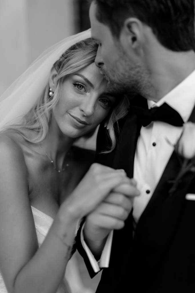 Black-and-white close-up portrait of a bride and groom embracing, with the bride resting her head against the groom while looking directly at the camera.
Soft focus and intimate framing create a quiet, emotional atmosphere.