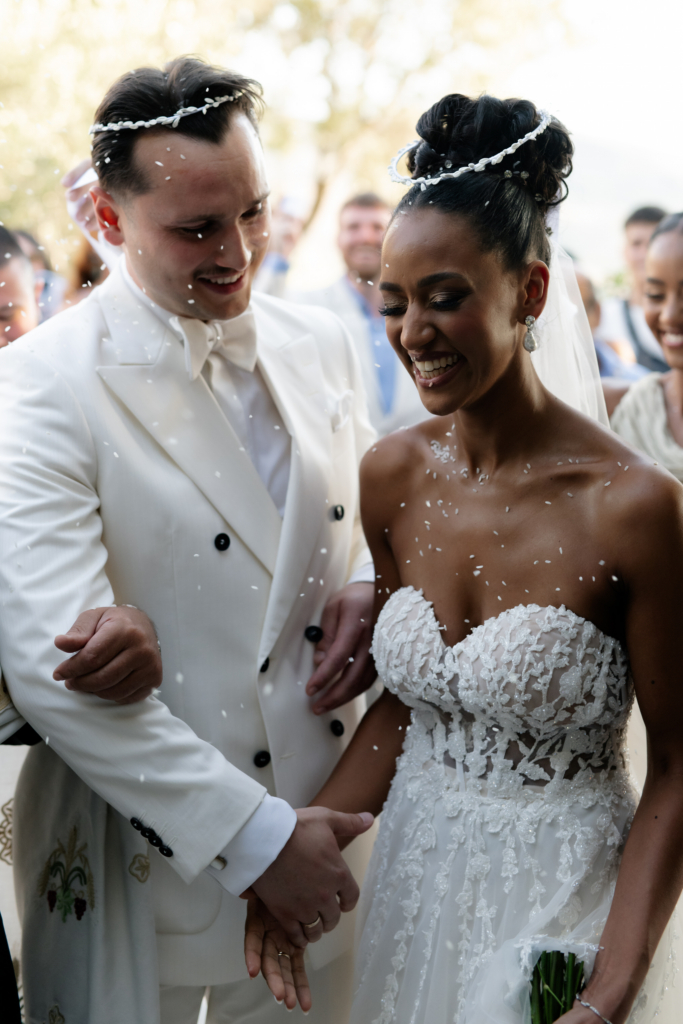 Bride and groom smiling and walking through a shower of white confetti moments after their wedding ceremony.
Guests surround the couple as they celebrate in bright natural light.