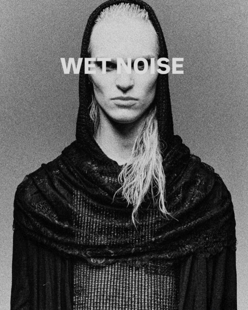 A bold black-and-white editorial portrait defined by texture, intensity, and presence. The wet hair, heavy draping, and raw grain create a stark visual language that feels both futuristic and primal, while the direct composition gives the image a strong, almost confrontational power.