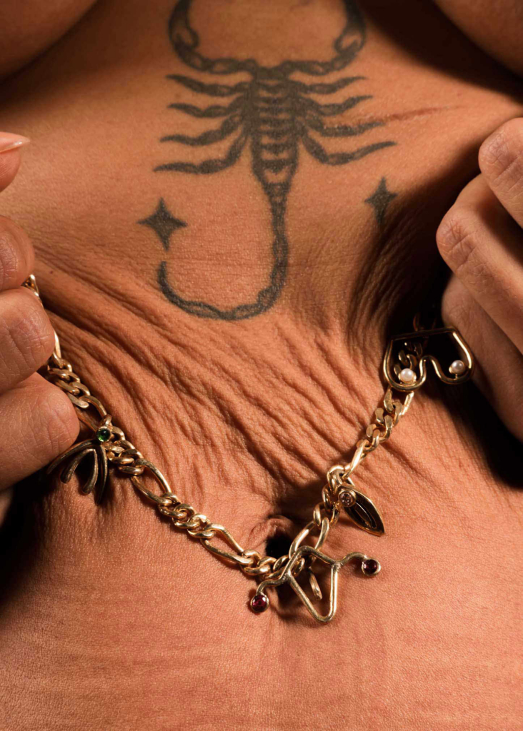 Close-up body detail with scorpion tattoo and sculptural jewelry composition