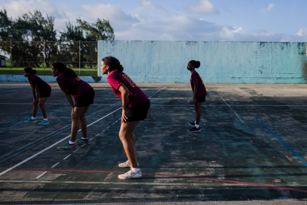 Teenage girls standing in defensive formation on an outdoor volleyball court during the Girls in Sport documentary photography project in Barbados.