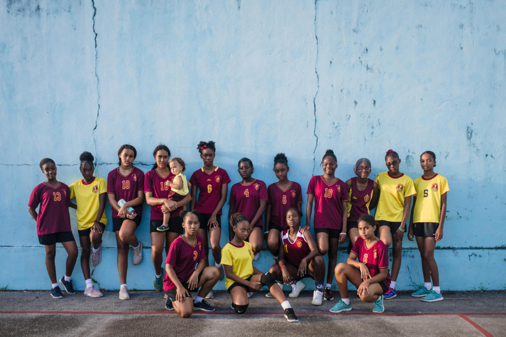 Group portrait of teenage girls from a volleyball team standing together against a blue wall during the Girls in Sport project in Barbados.