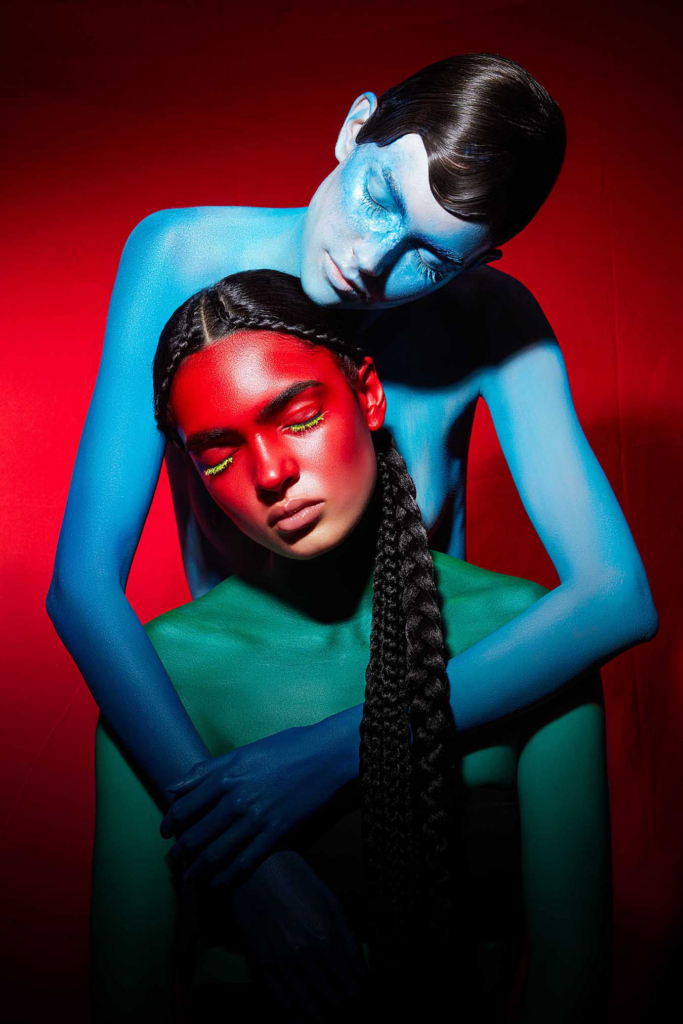 Surreal double portrait with painted bodies, braided hair, and intense complementary color contrast.