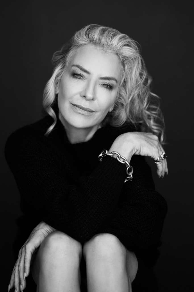 Black and white studio portrait of a woman with silver hair resting her arm gently across her knee.
