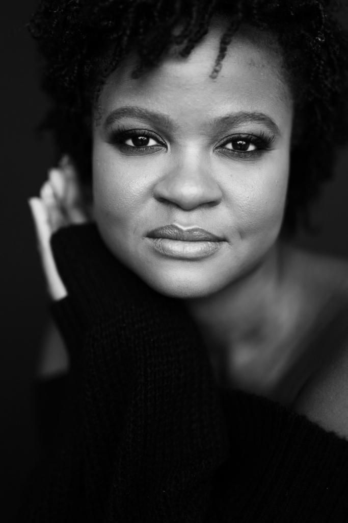 Close-up black and white portrait of a woman with natural textured hair looking directly into the camera.