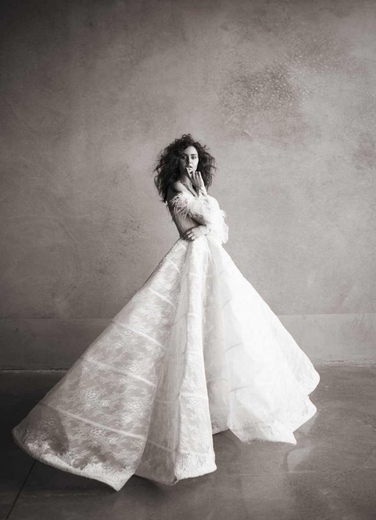 A woman stands in a dramatic white couture gown with a wide flowing skirt against a textured studio backdrop.
Soft monochrome tones and elegant posing create a timeless high-fashion portrait.