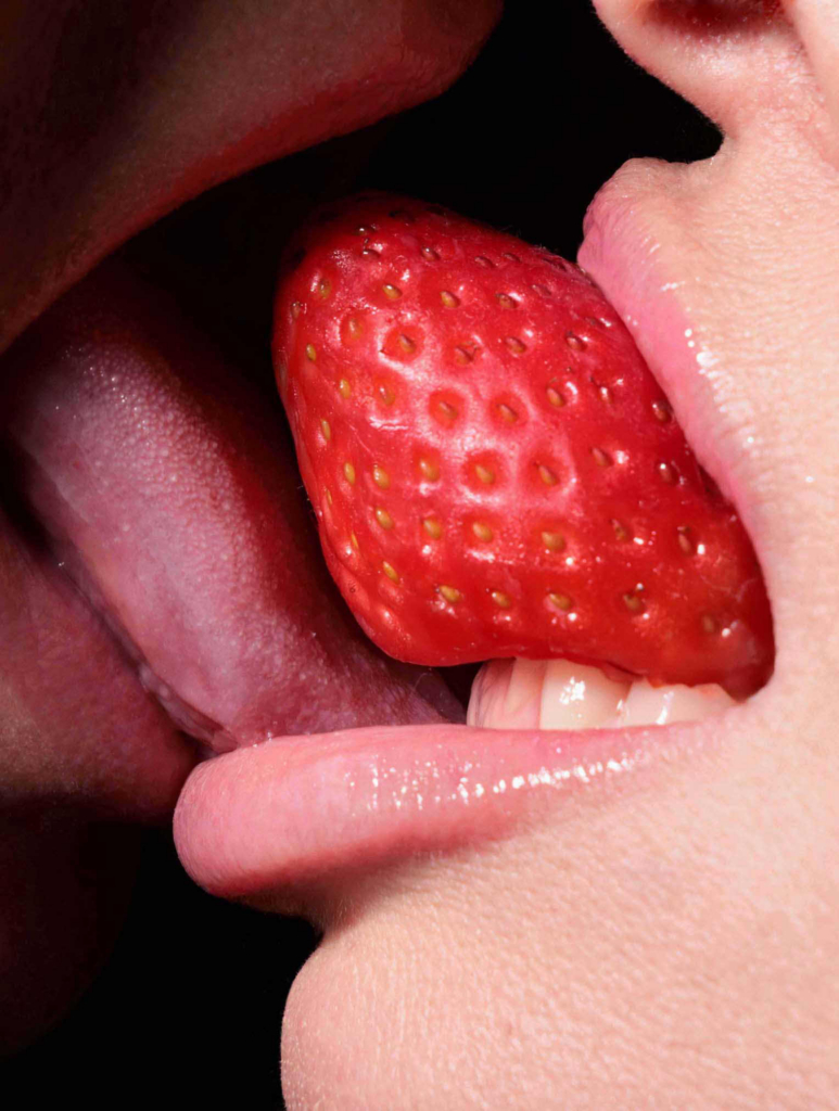Sensual close-up of lips, tongue, and strawberry in a bold erotic food composition.