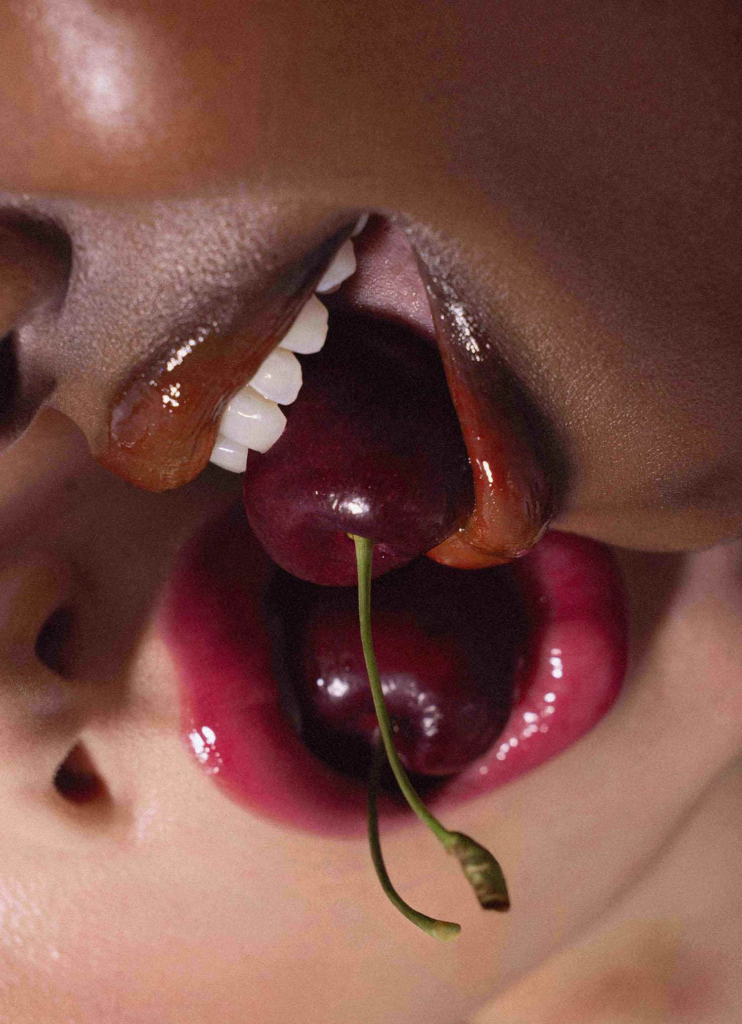 Erotic close-up blending glossy lips, teeth, and cherries into a sensual still life composition.