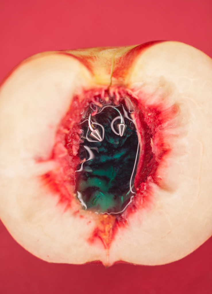 Dreamlike macro still life of a split peach with liquid-filled center, vivid pink and coral tones, organic textures, and surreal editorial aesthetic.