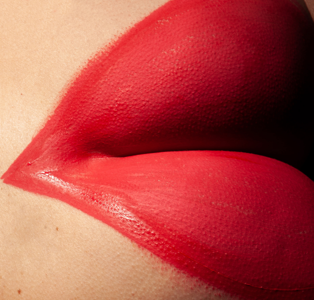 Extreme beauty macro of vivid matte red lips, hyper-detailed skin texture, editorial fashion photography, dramatic studio lighting, saturated crimson tones, minimal composition, sensual abstract close-up, luxury cosmetic campaign aesthetic.