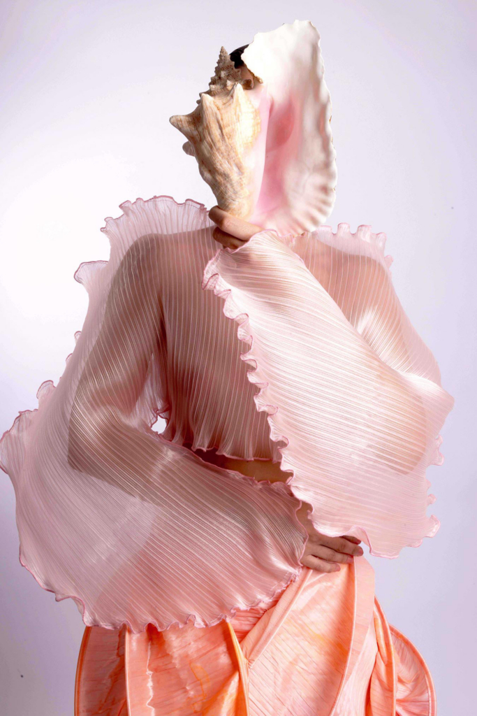 Conceptual fashion portrait with pleated pastel textures and seashell-inspired sculptural styling.