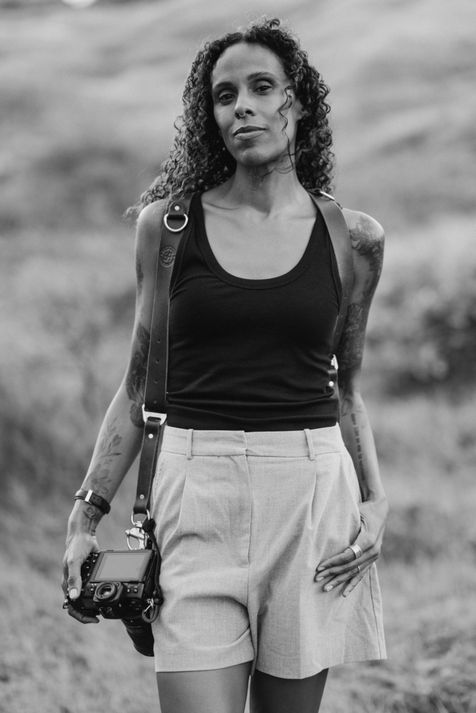 Portrait of photographer Aniya Emtage Legnaro holding a camera in an open field during an outdoor documentary portrait session.