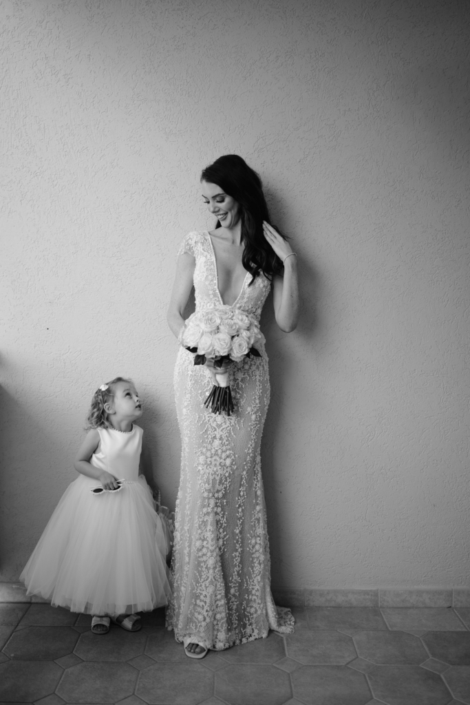 Bride holding a bouquet while a flower girl looks up at her during a candid wedding portrait.