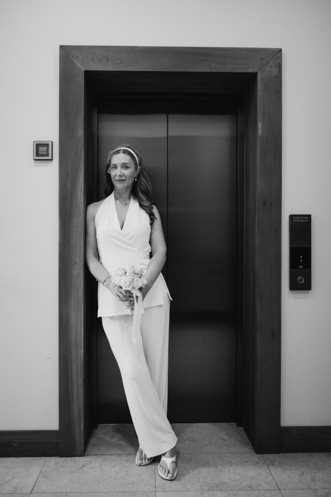Bride standing in an elevator doorway holding her bouquet before the wedding ceremony.